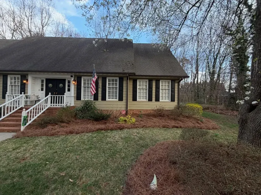 Suburban house with front porch, white railings, and American flag, surrounded by winter landscaping.