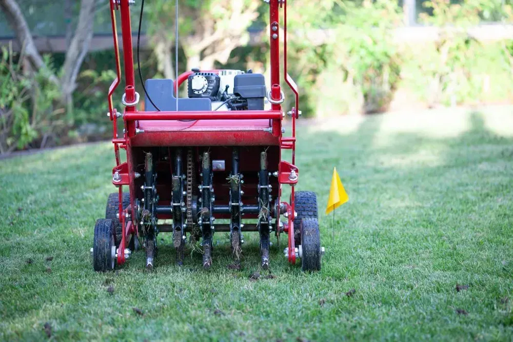 Red agricultural machine on grass, with multiple wheels and a yellow flag in a sunny field.