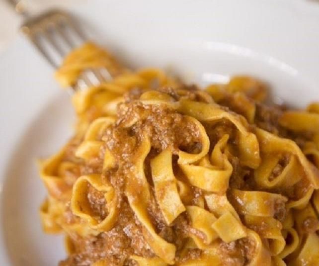 Pasta al ragù su un piatto bianco, con la forchetta nel cibo.