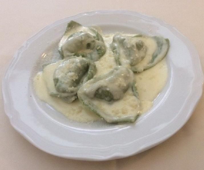 Pasta verde ripiena di formaggio in una cremosa salsa bianca su un piatto bianco.