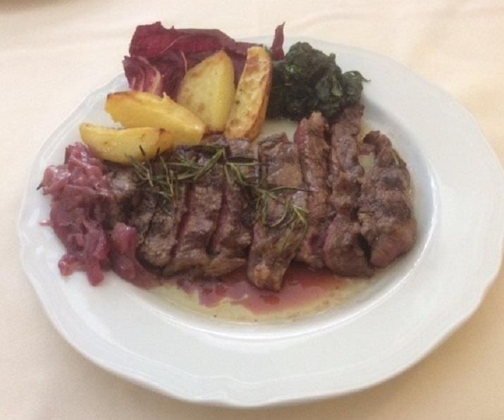 Bistecca tagliata a fette con patate, cavolo rosso, spinaci e radicchio su un piatto bianco.