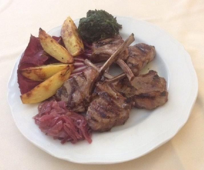 Costolette di agnello alla griglia con patate arrosto e cavolo rosso su un piatto bianco.