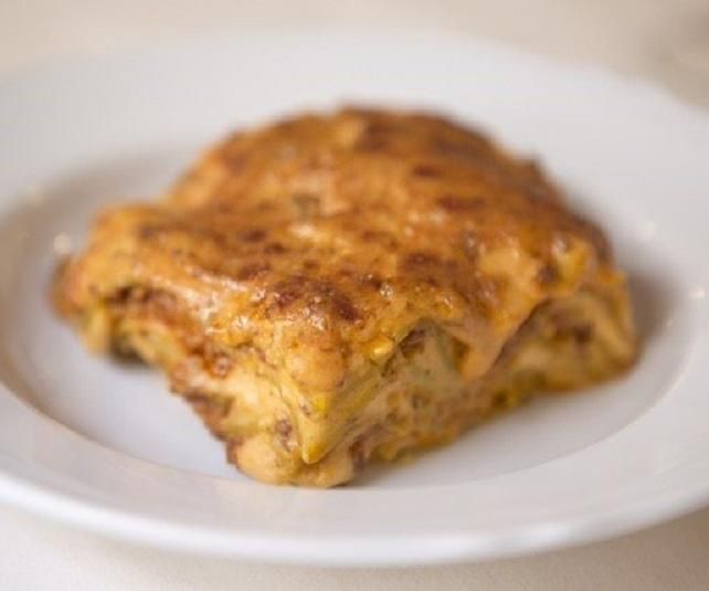 Lasagna su un piatto bianco; superficie dorata al forno.