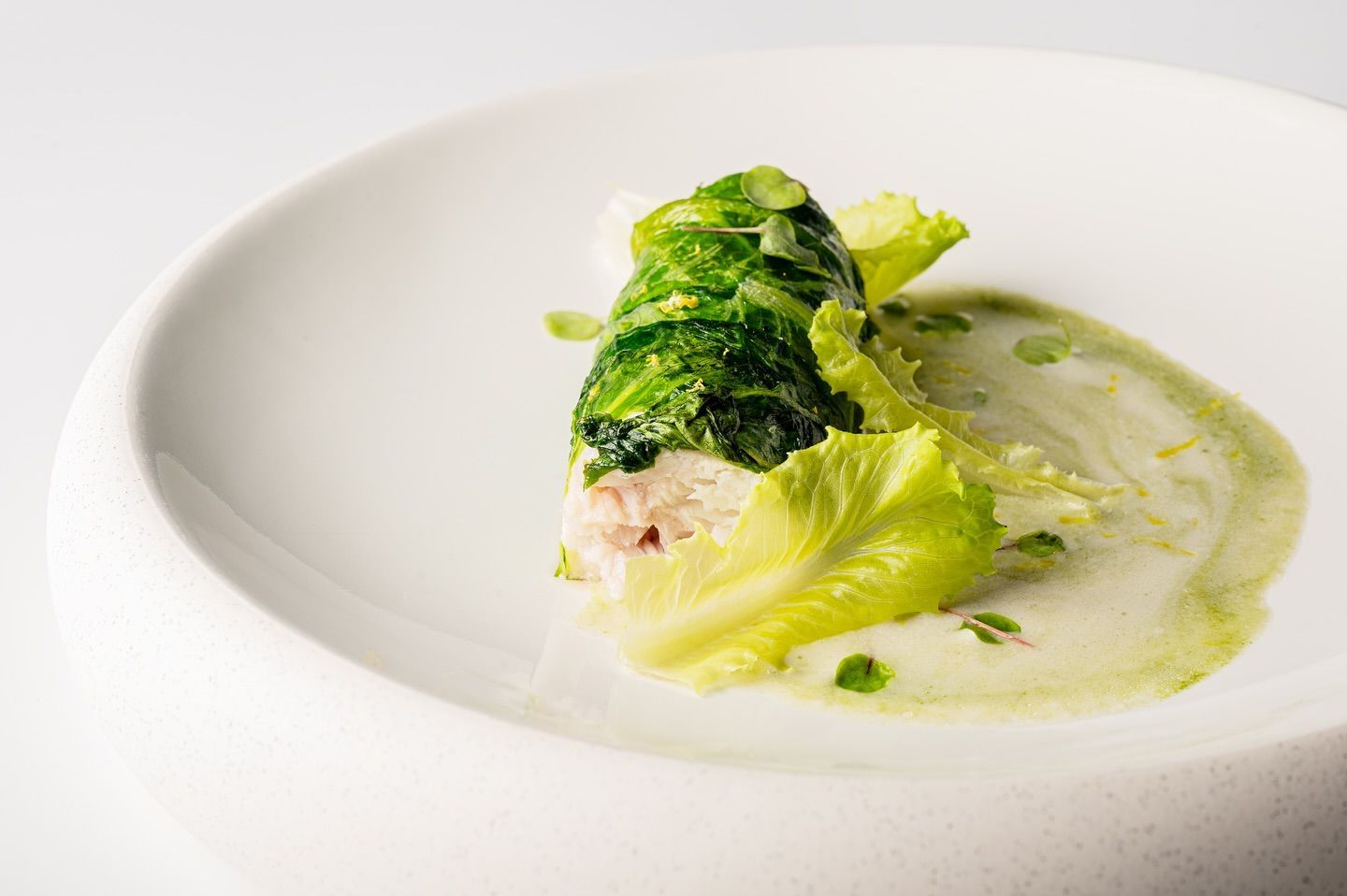 Involtino di cavolo su un piatto bianco con salsa verde e lattuga.