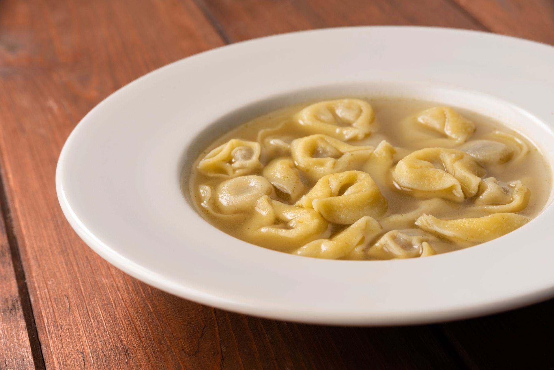 Zuppa di tortellini in una ciotola bianca su un tavolo di legno.