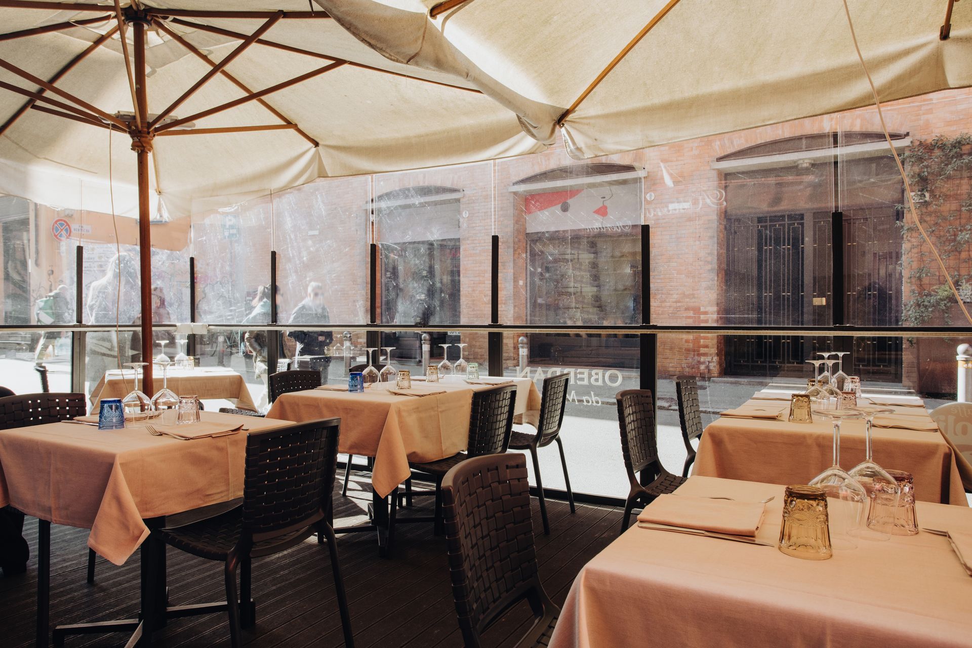 Patio del ristorante con tavoli apparecchiati per cenare, sotto un ombrellone. La luce del sole filtra a fiotti.