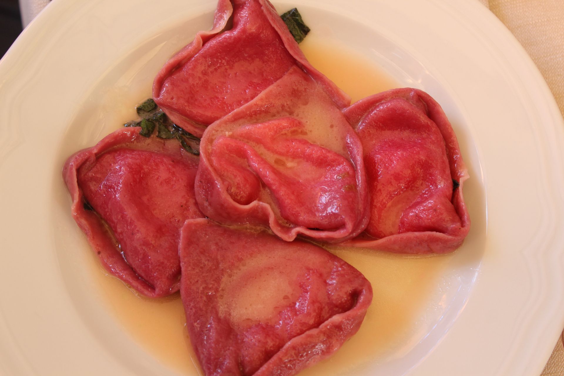 Ravioli rosa in salsa leggera su un piatto bianco.