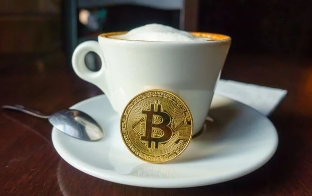 A cup of coffee with a gold coin with the letter b on it