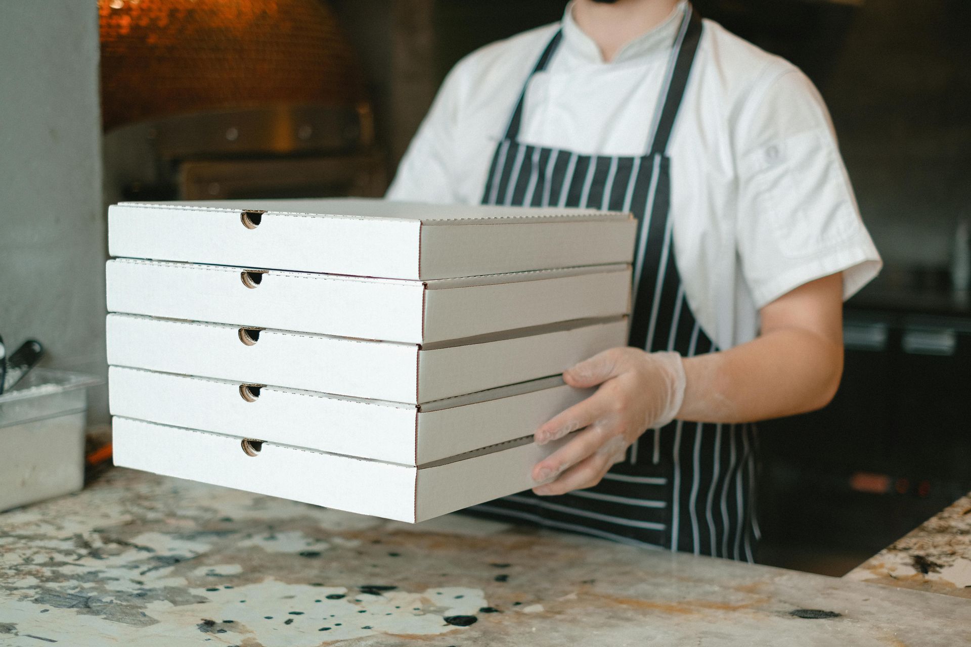 A man in an apron is holding a stack of pizza boxes.