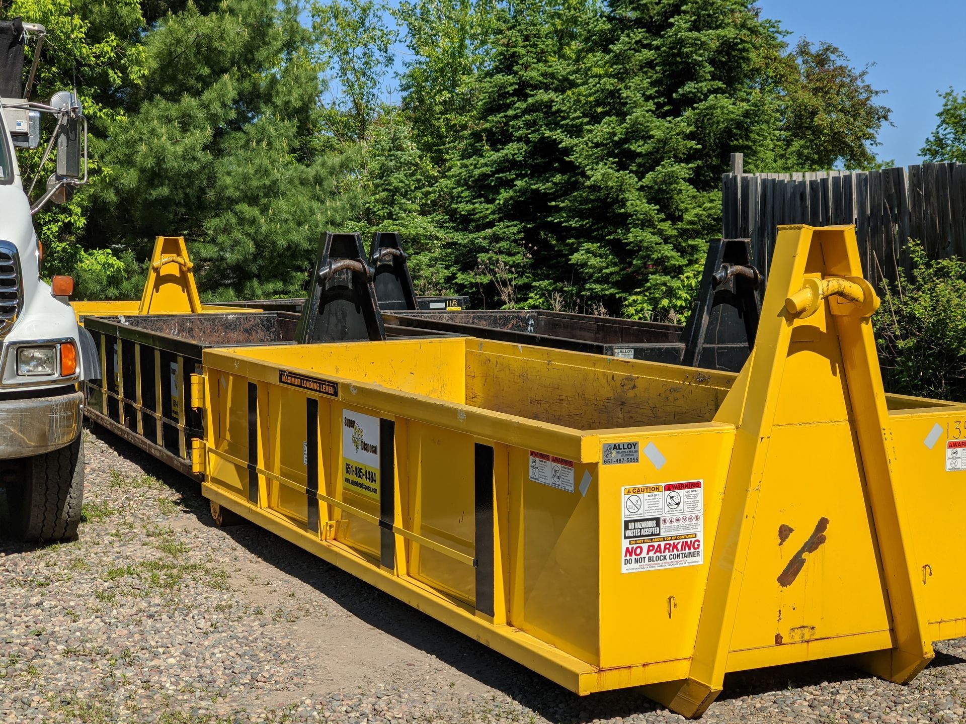 A yellow dumpster is parked next to a white truck.