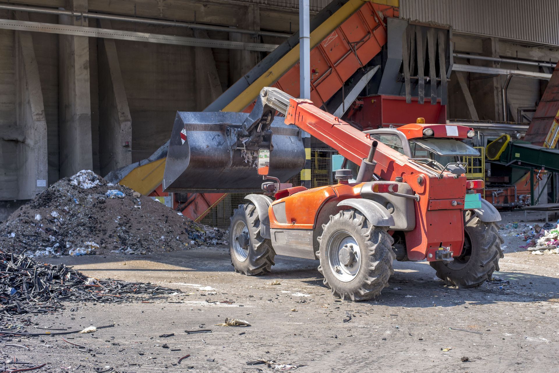 A red tractor is loading a pile of rocks into a conveyor belt.