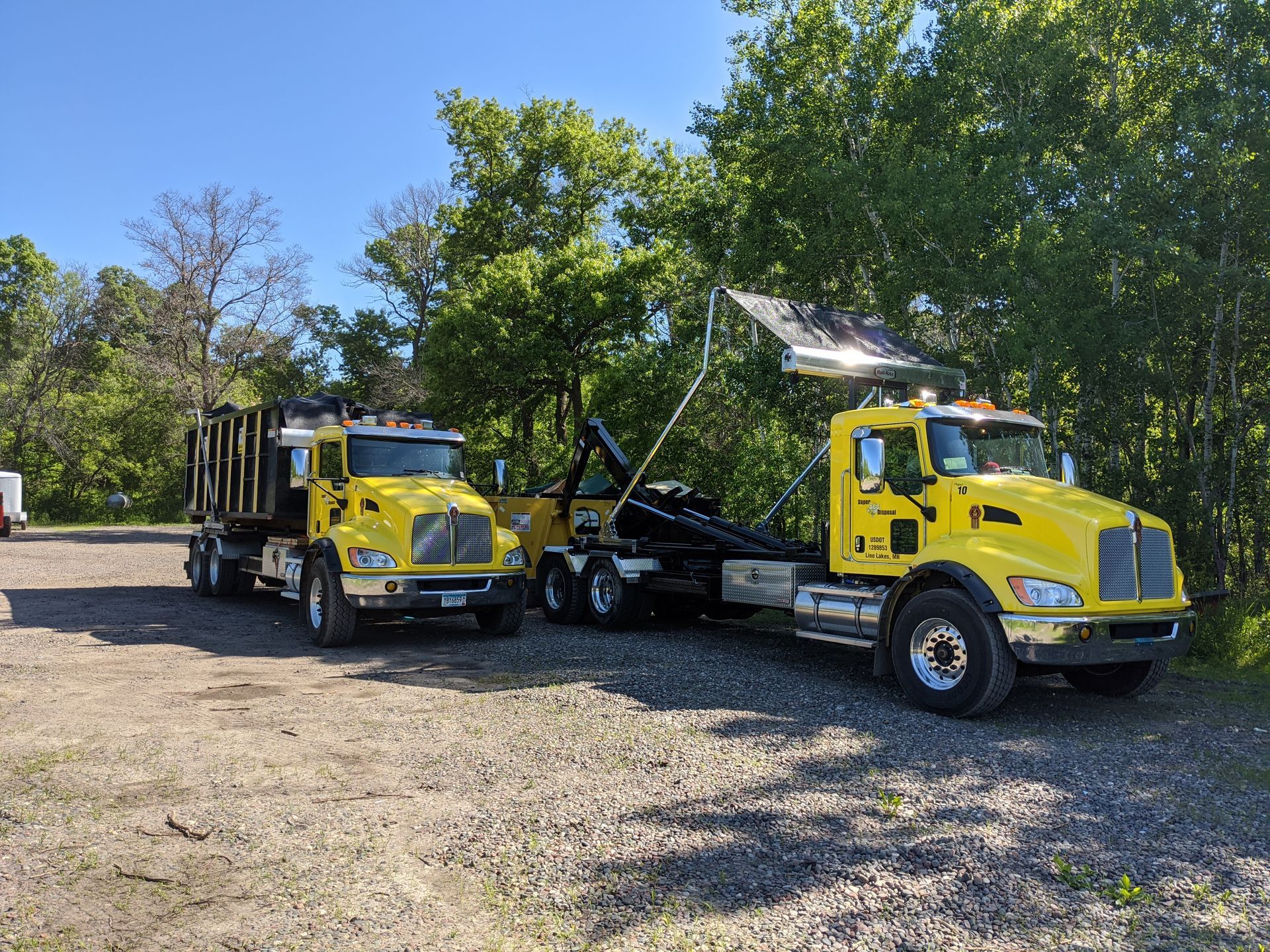 Two yellow dump trucks are parked next to each other in a gravel lot.