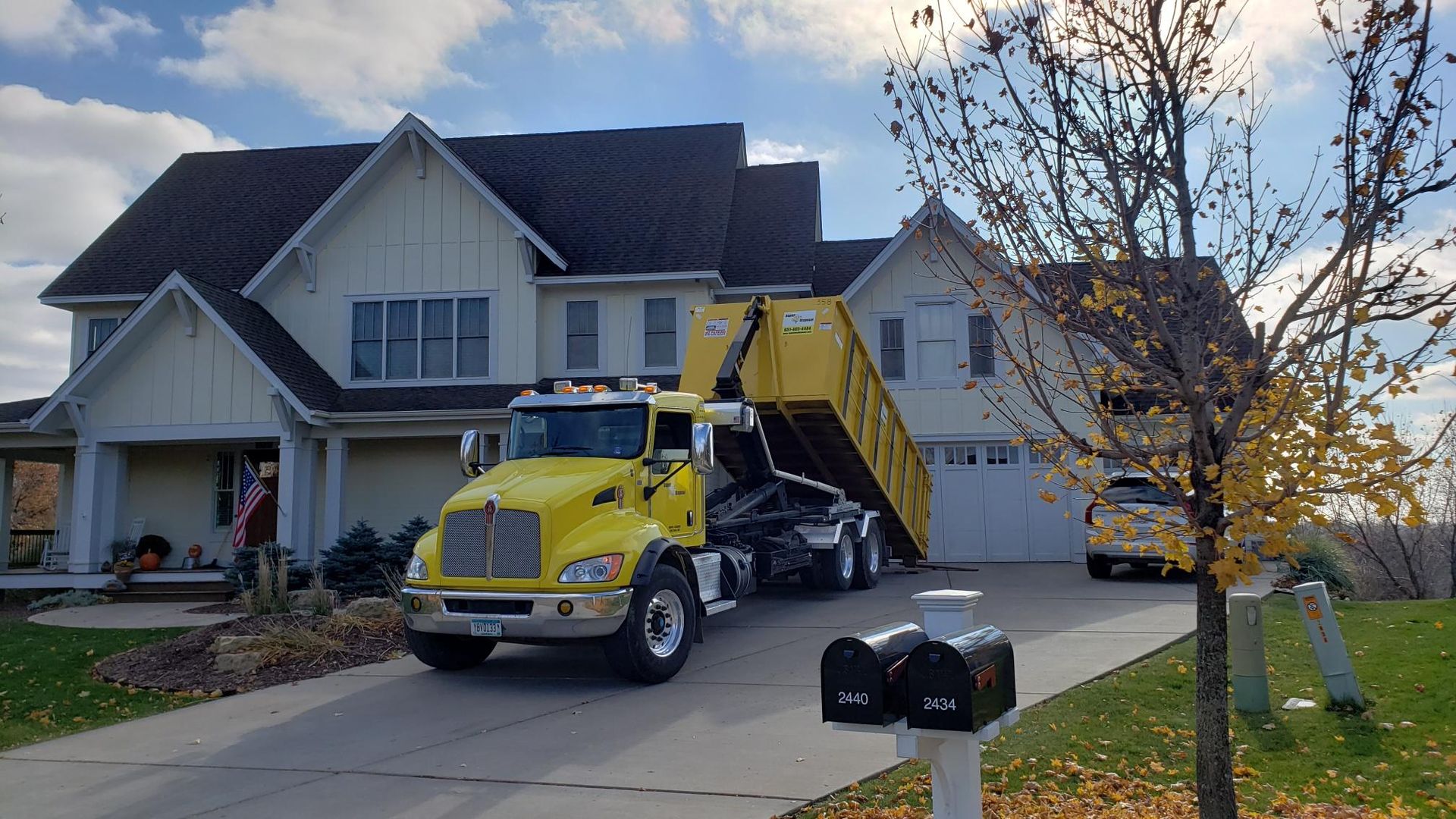 A yellow dump truck is parked in front of a large house.