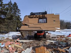 a skid steer is lifting a house in the snow
