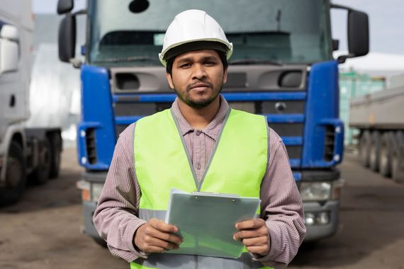 a man wearing a hard hat is holding a clipboard in front of a truck