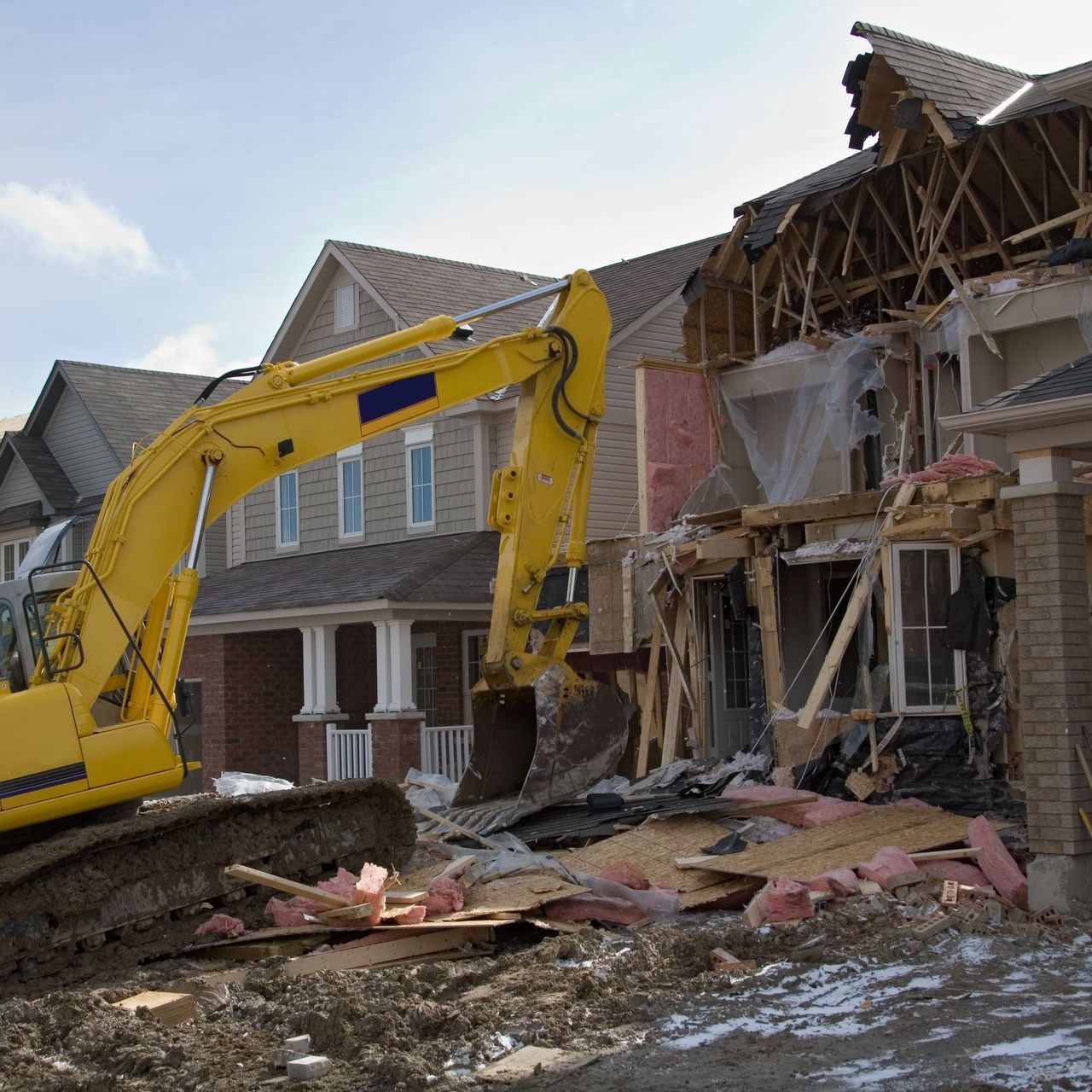 A yellow excavator is demolishing a house in a residential area.