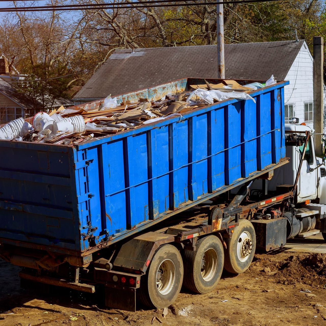 A dump truck is carrying a blue dumpster full of trash.