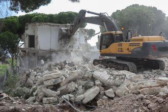 A yellow and black excavator is demolishing a building