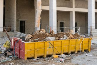 A large yellow dumpster is sitting in front of a building under construction.