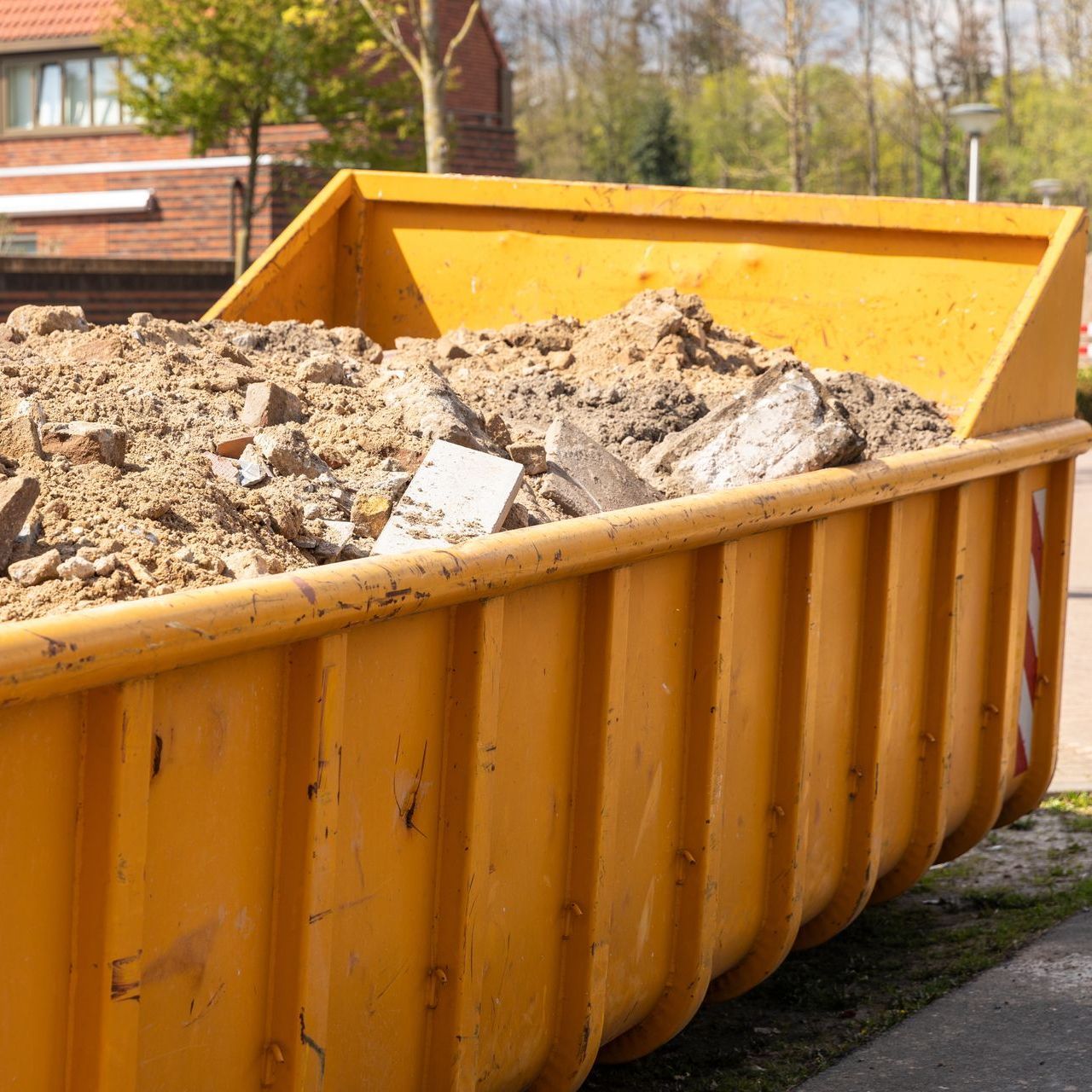 A yellow dumpster filled with dirt is parked on the side of the road.