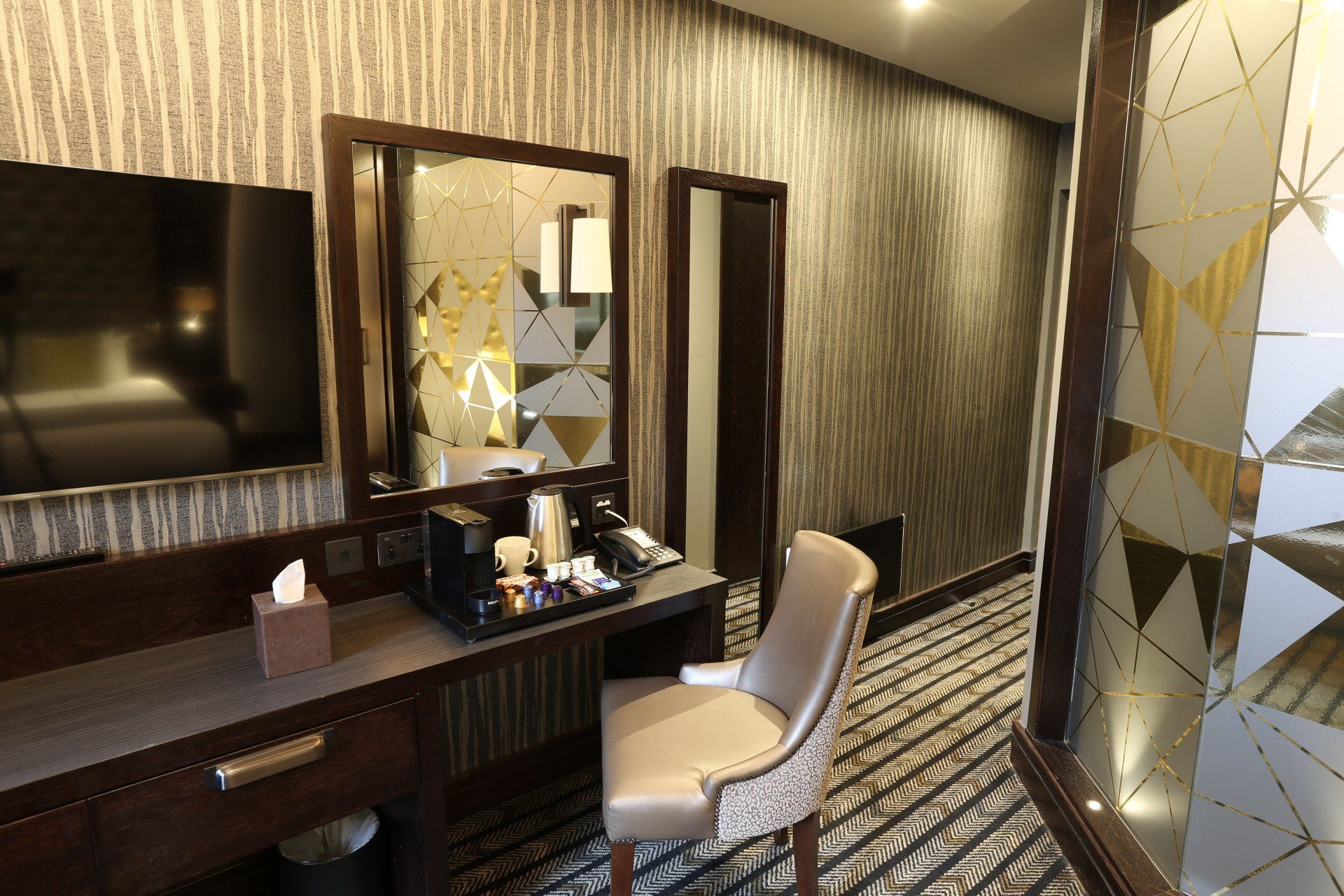 Bedroom vanity with a mirror, desk, chair, and TV. Brown and gold tones.