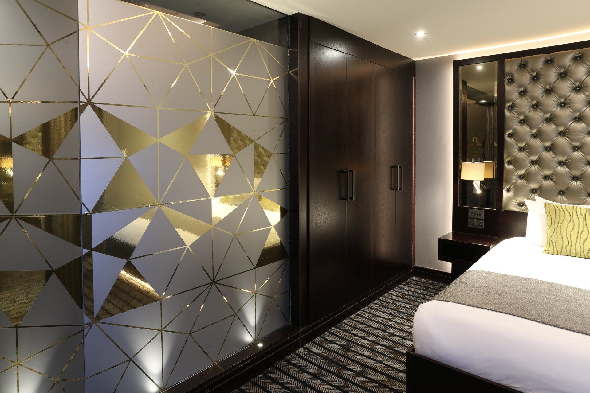 Modern hotel room with frosted glass design, dark wood closet, and tufted headboard.