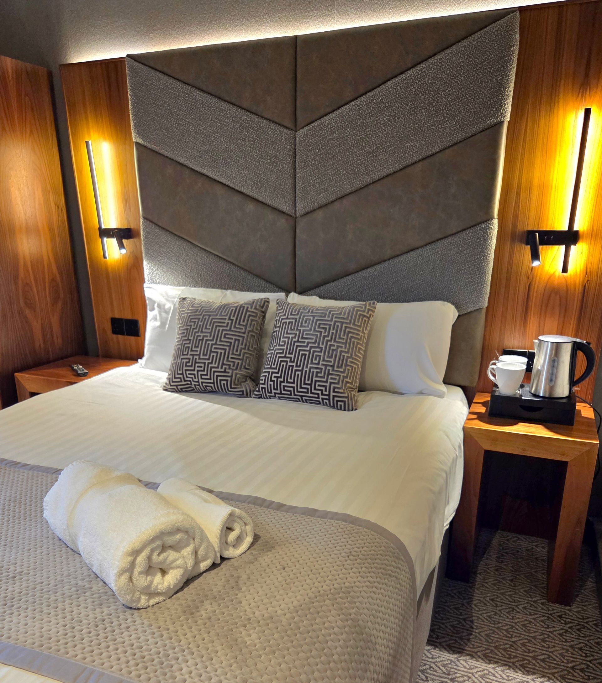 Hotel bedroom with a bed, a window, and a wardrobe. Brown wooden paneling.
