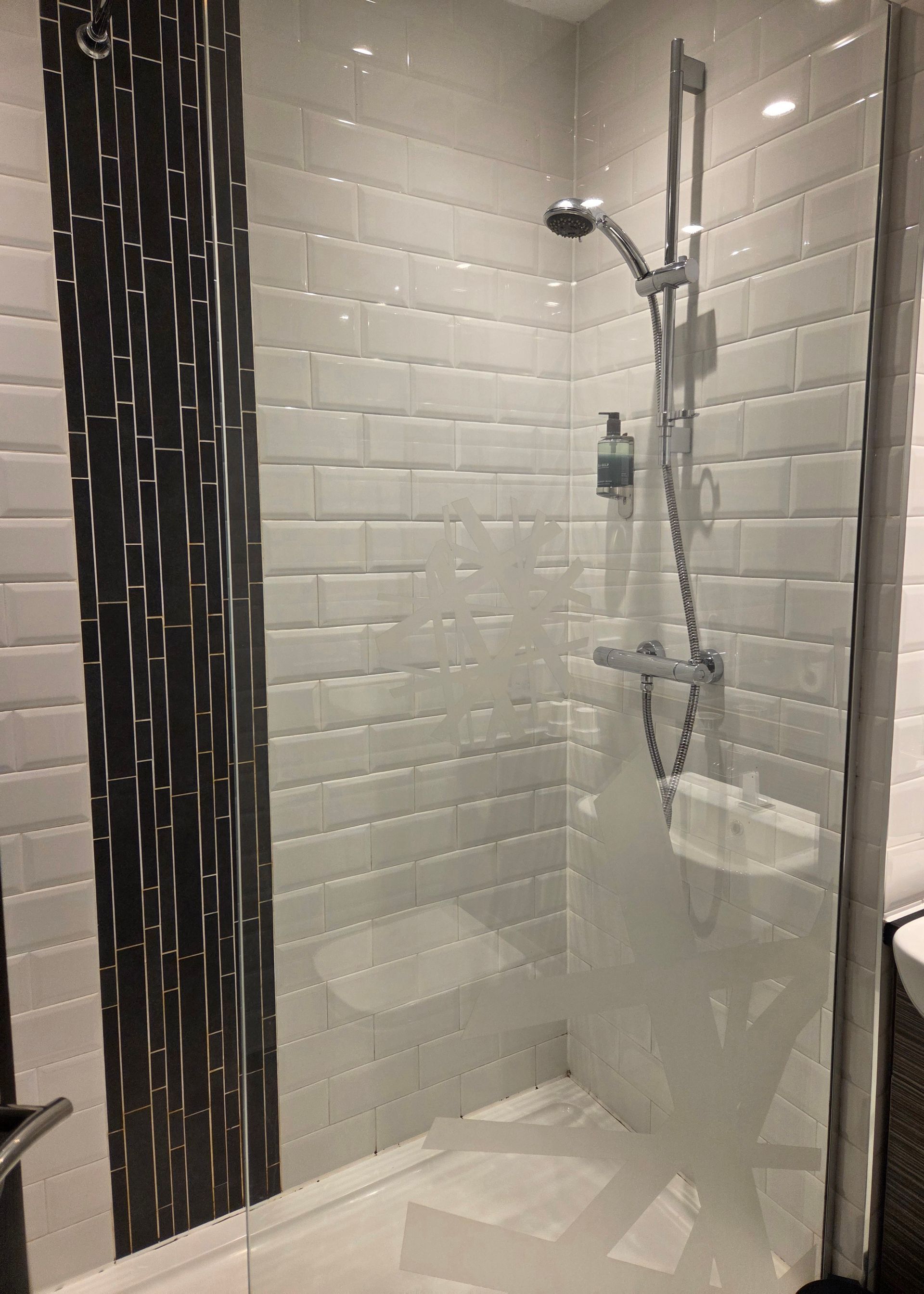 Bacon sandwich on a white plate with teacup, milk jug, and ketchup, on a wooden table.