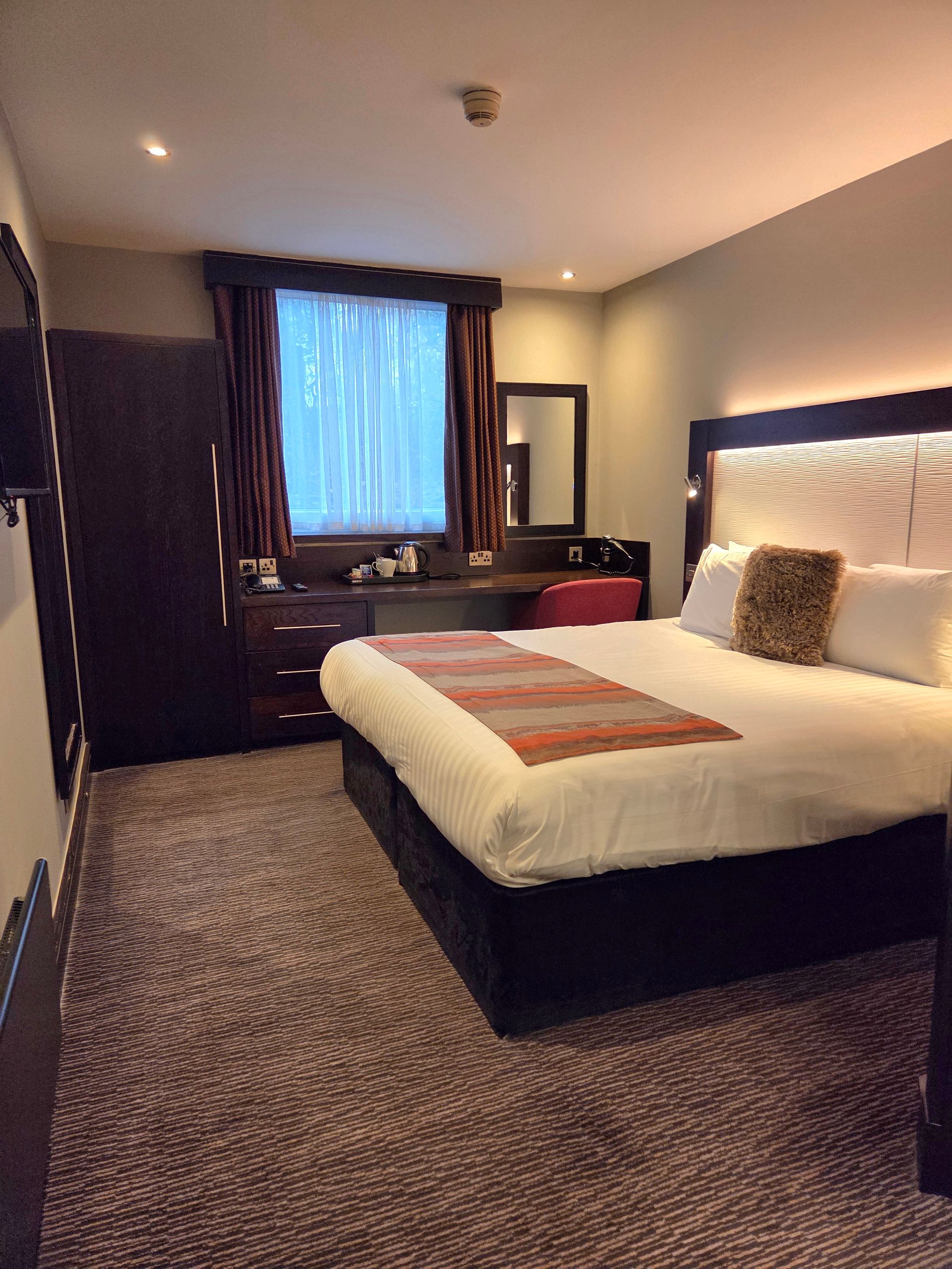 Hotel bedroom with a bed, a window, and a wardrobe. Brown wooden paneling.