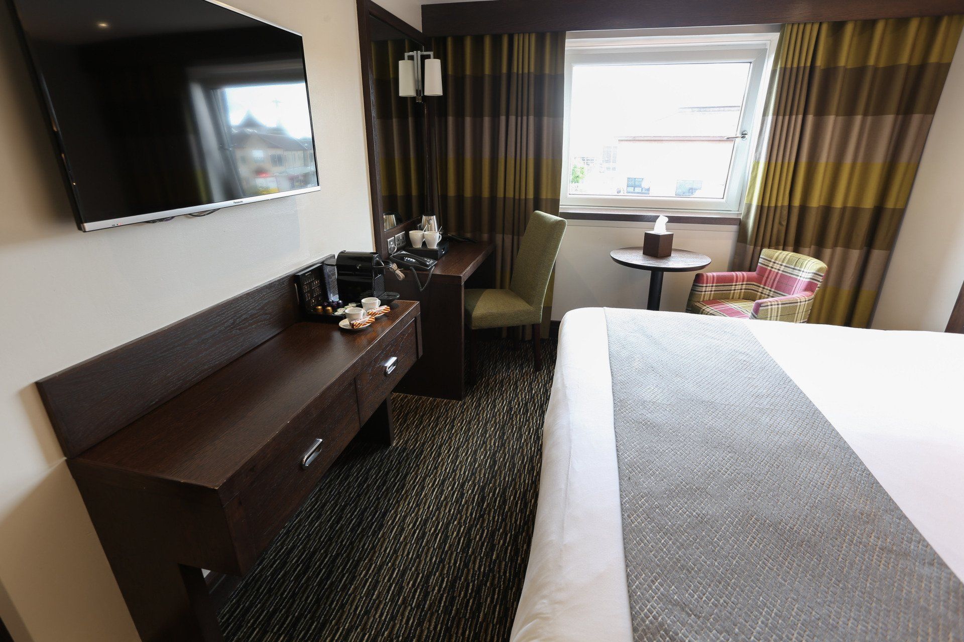 Hotel room with bed, desk, TV, and window with patterned curtains.