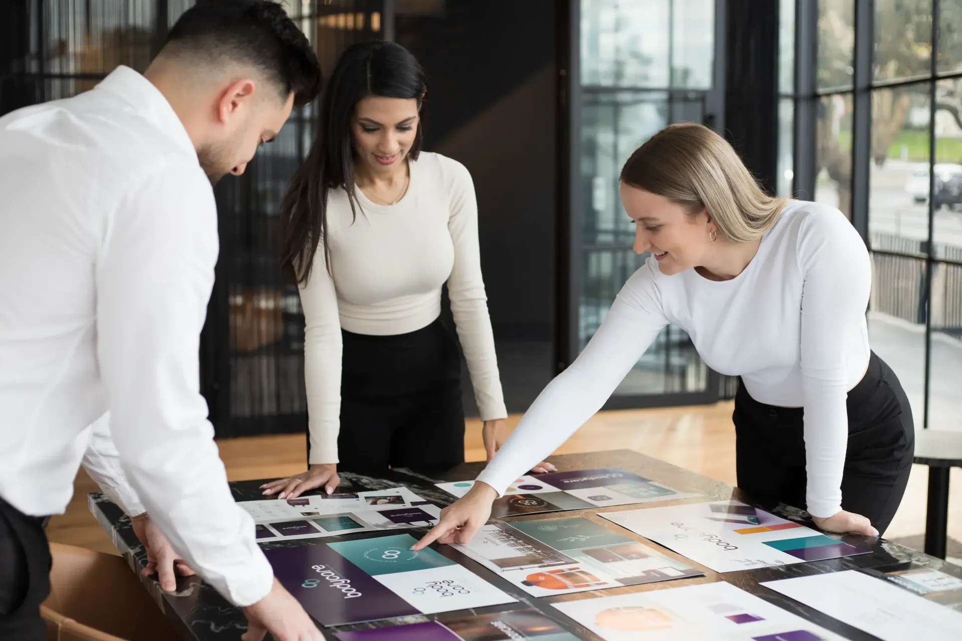Three business people reviewing design layouts around a large table.