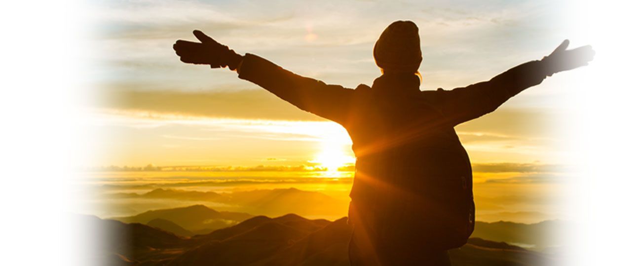 a person is standing on top of a mountain with their arms outstretched at sunset .