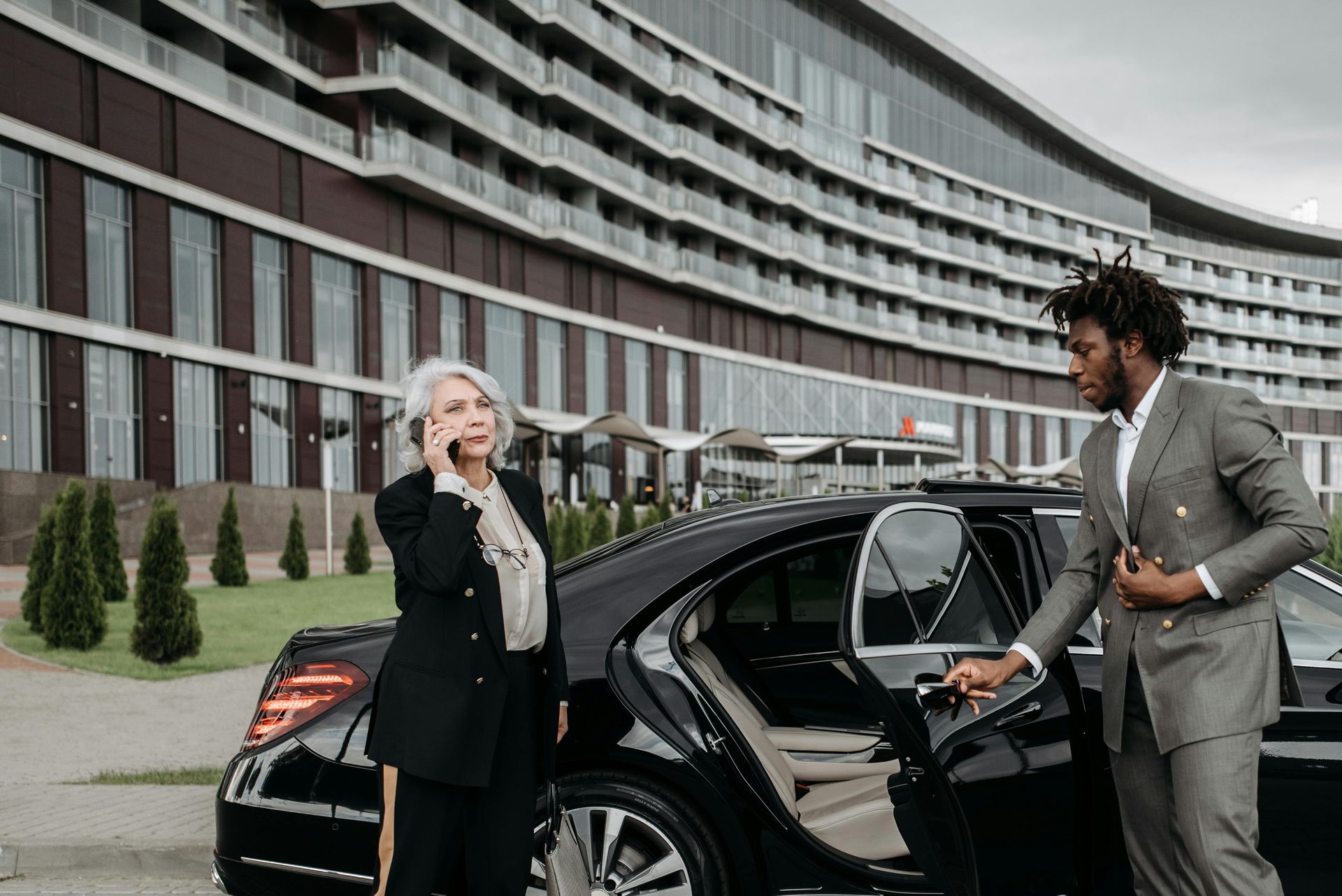 Woman on phone near a car, man opening door in front of a building.