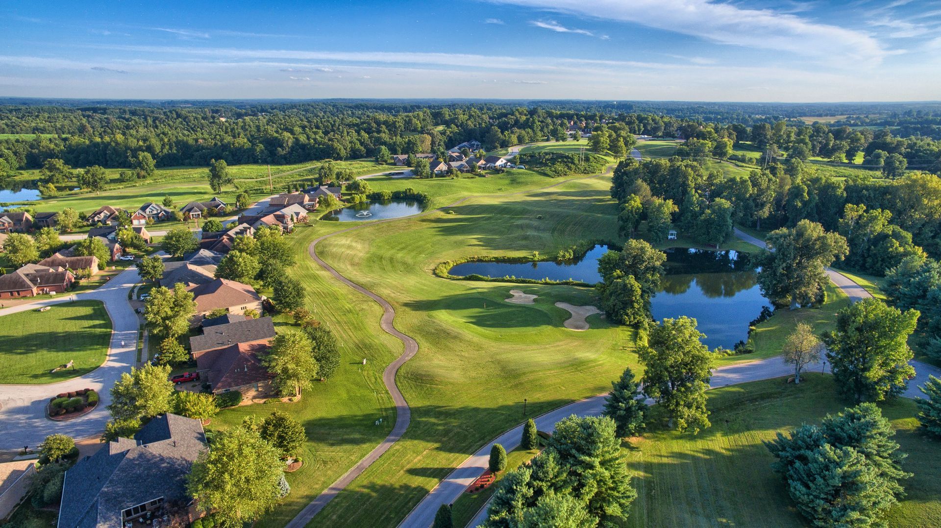 An aerial view of a golf course surrounded by trees and houses.