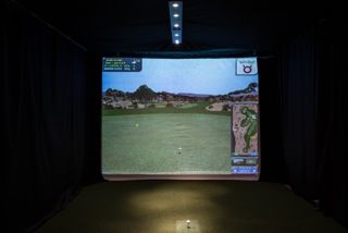 A golf game is being played on a screen in a dark room.