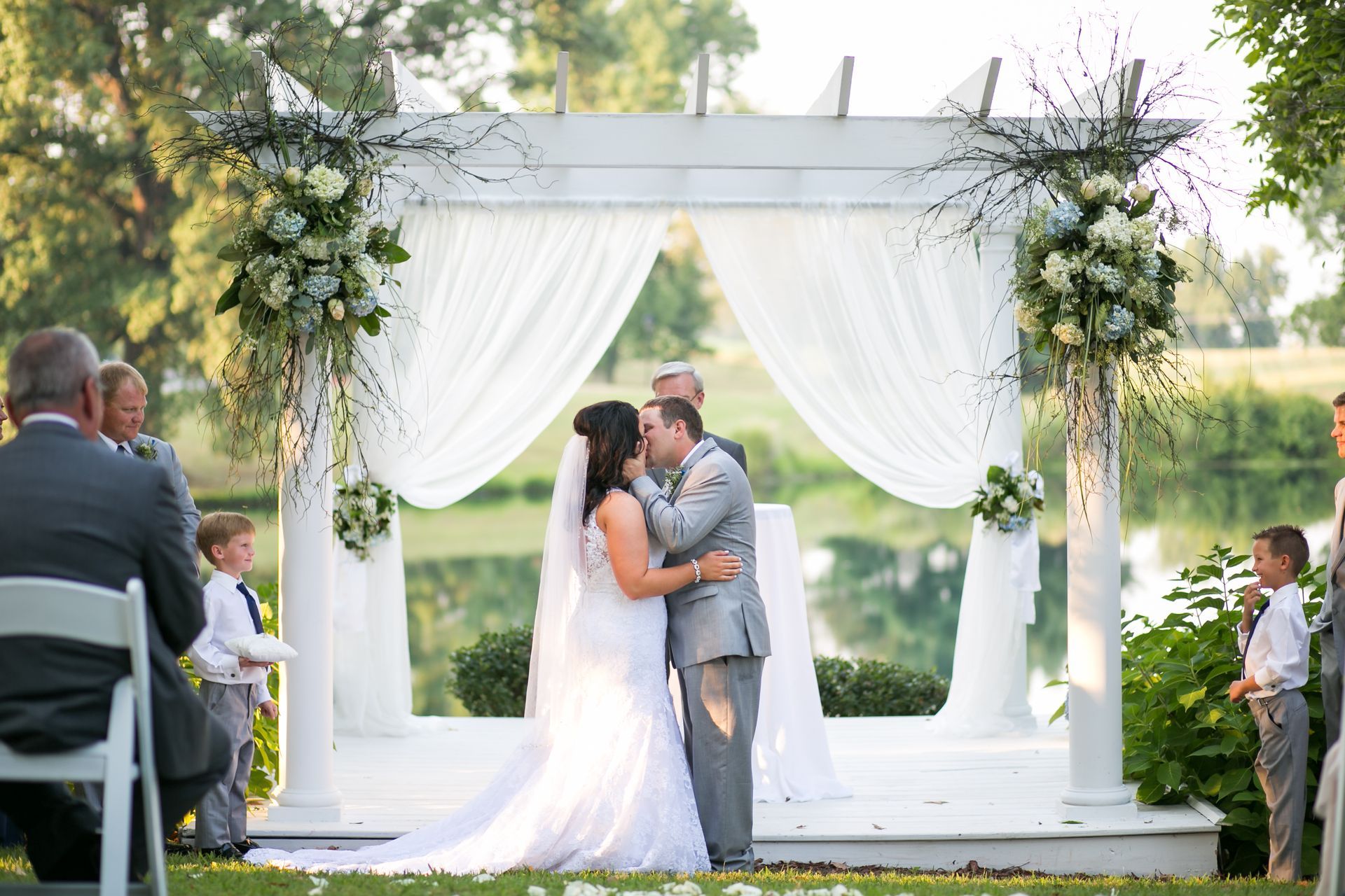 A bride and groom are kissing under a white pergola at their wedding ceremony.