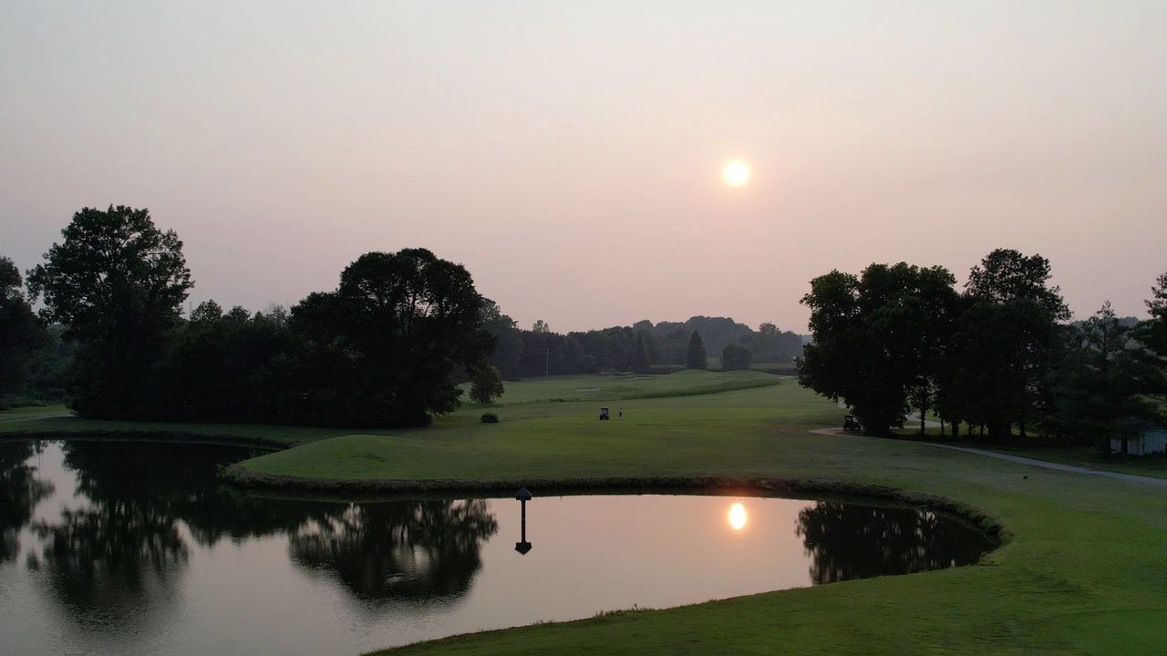 The sun is setting over a golf course with a lake in the foreground