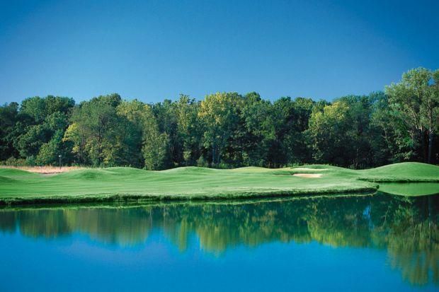 A golf course with a lake in the foreground and trees in the background.