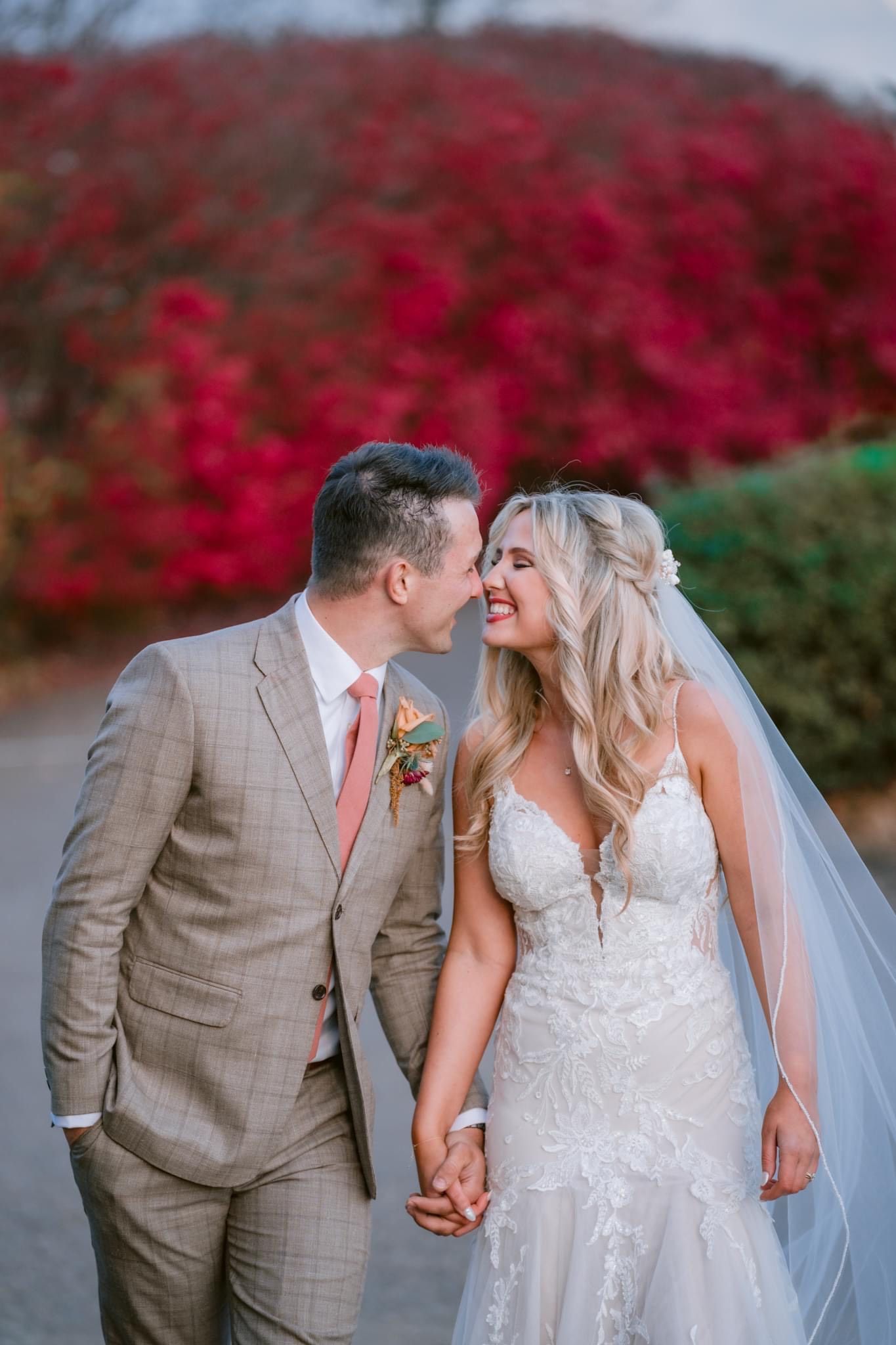 A bride and groom are kissing in front of a bush with red leaves.