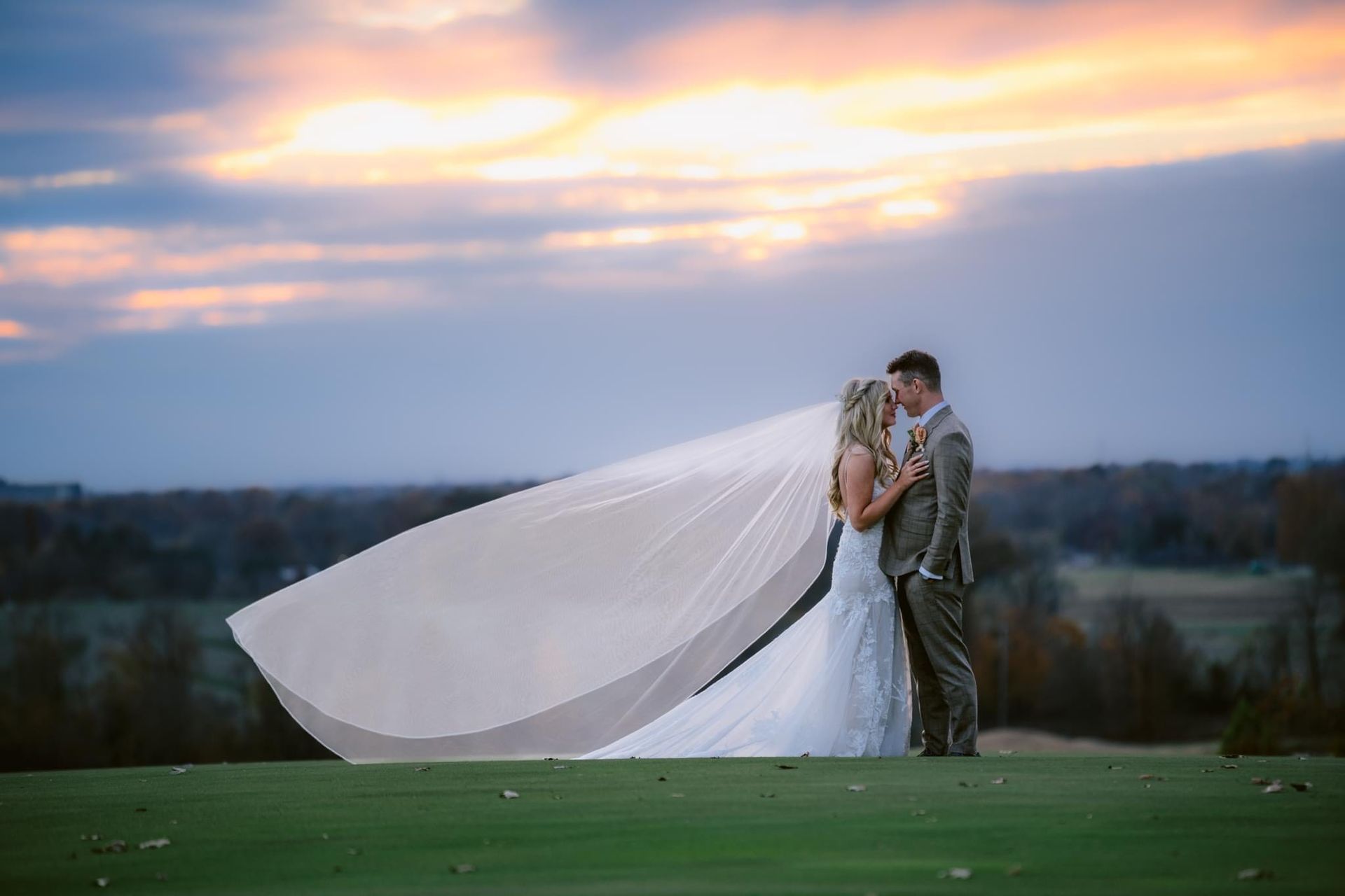 A bride and groom are kissing on a golf course with a veil blowing in the wind.