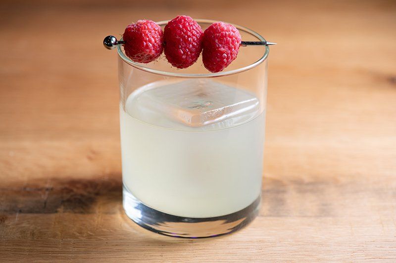 A glass of water with raspberries on a toothpick on a wooden table.