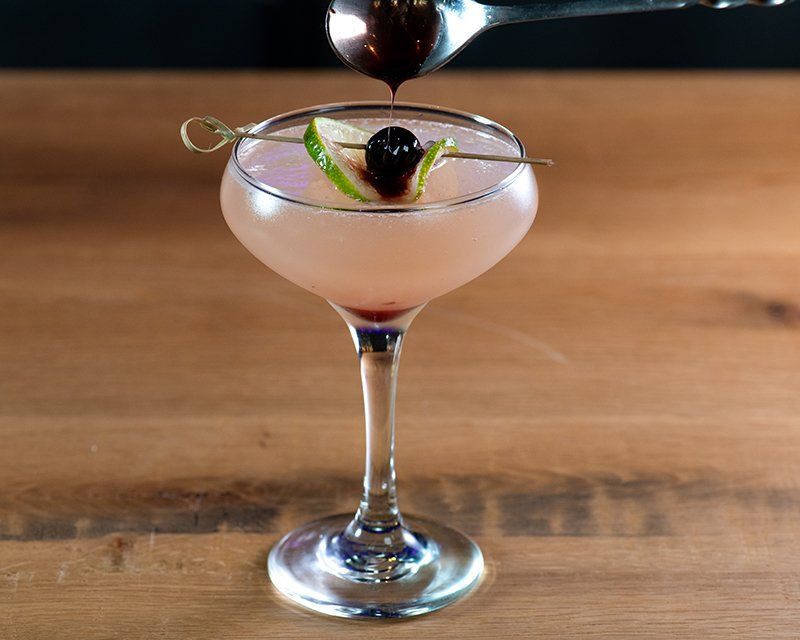 A martini is being poured into a glass on a wooden table