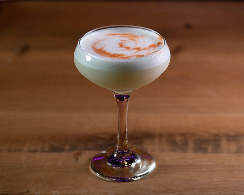 A close up of a cocktail in a wine glass on a wooden table.