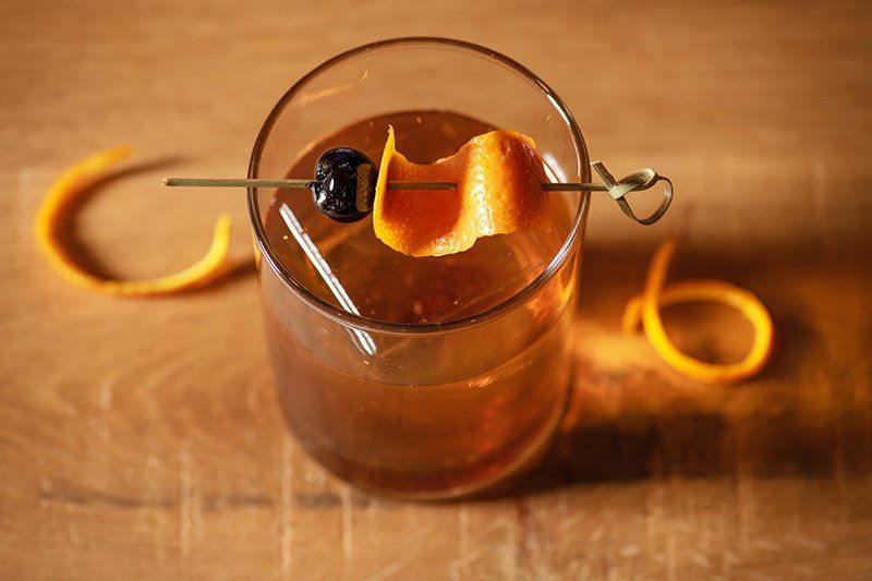 A glass of whiskey with a cherry and orange peel on a toothpick.