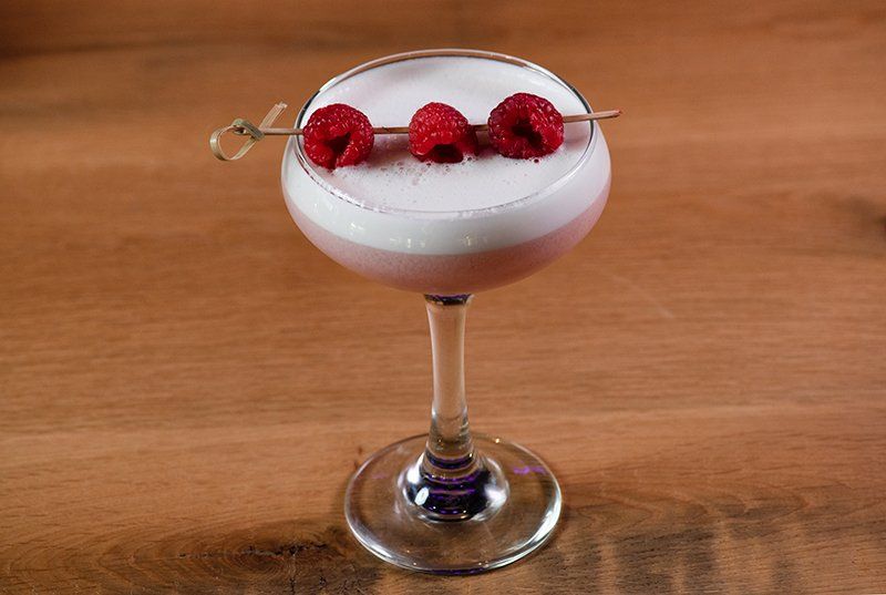 A martini glass with raspberries on top of it on a wooden table.