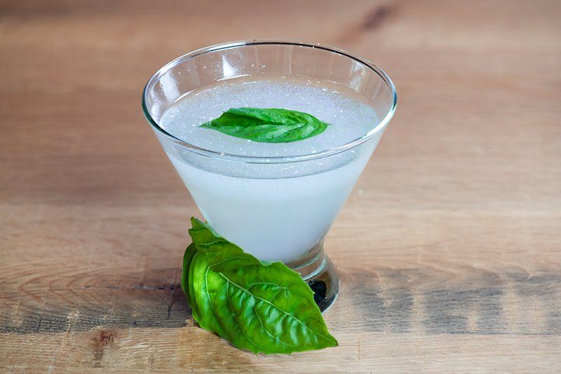 A martini glass with a basil leaf on top of it on a wooden table.