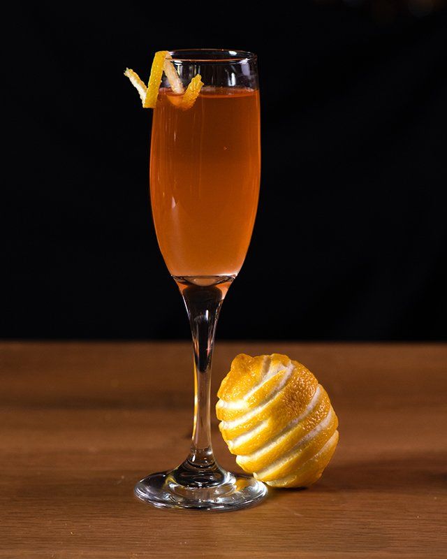 A champagne glass filled with a drink next to a lemon on a wooden table.