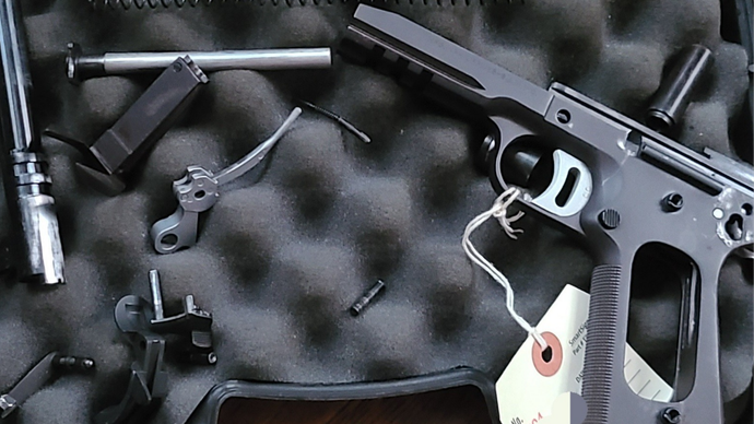 Black firearm parts arranged in a foam-lined case, with a cable lock attached.