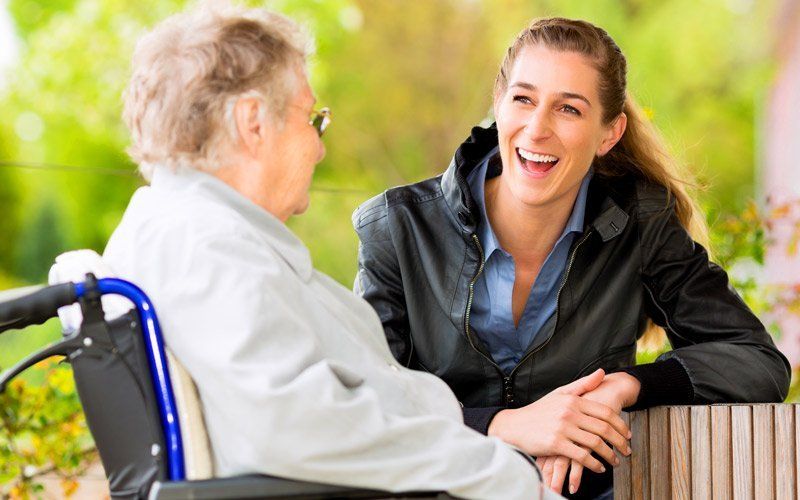 An elderly woman in a wheelchair is talking to a young woman.