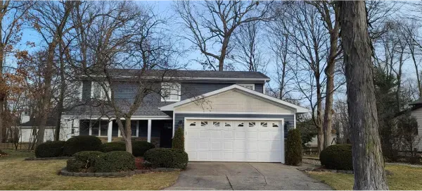 A house with a white garage door is surrounded by trees and bushes.